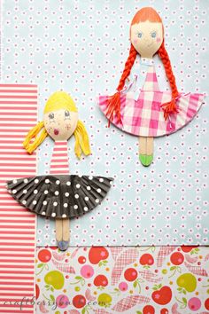 two paper dolls are sitting on top of a piece of fabric, and one is wearing a dress