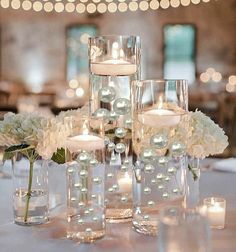 the centerpieces are filled with white flowers and lit candles in glass vases