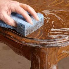 a hand with a sponge on top of a wooden bench that has been stained brown