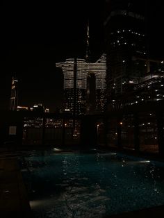 an empty swimming pool in the middle of a city at night with skyscrapers lit up