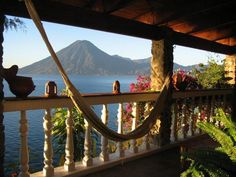 there is a hammock hanging on the porch next to the water and mountains