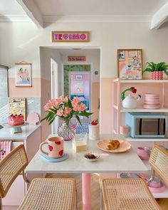 a kitchen with pink walls and wooden chairs around a white table topped with plates, cups and vases filled with flowers