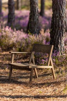 a wooden bench sitting in the middle of a forest filled with purple wildflowers