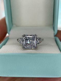 New in 2023! This stunning engagement ring features a magnificent 5CT(10mm*10mm)  square radiant cut crushed ice simulated diamond center stone with clear crushed ice simulated diamonds on each size of the shank. Available with 3Ct stone at this link: https://www.etsy.com/listing/1347871521/ It is perfect for someone who wants an extravagant and unique engagement ring, or just a beautiful ring for someone who loves jewellery. ---------------------------------------------- MATERIALS: Sterling Silver 925 plated with rhodium  Crushed ice CZ simulated diamond center stone: 5CT (10mm*10mm) Side stones:  crushed ice clear CZ diamonds  Ring size fit: Standard American size fit. If you're half size I would recommend to go with half size down. ---------------------------------------------- Will com Silver Moissanite Diamond Ring Rectangular, Three Stone Cubic Zirconia Diamond Ring Princess Cut, Princess Cut Three Stone Cubic Zirconia Diamond Ring, Three Stone Princess Cut Cubic Zirconia Ring, Three Stone Rectangular Diamond Jewelry, Rectangular Three Stone Diamond Jewelry, Silver Three Stone Asscher Cut Jewelry, Diamond White Radiant Cut Three Stone Jewelry, Rectangular Three Stone Diamond Ring