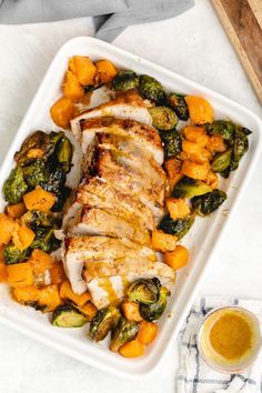 chicken, squash and brussel sprouts on a white platter next to a glass of orange juice