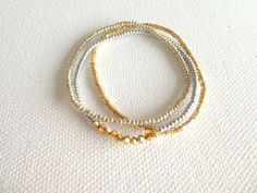 three beaded bracelets with gold and silver beads on a white cloth covered surface