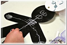 a person is drawing on a black piece of paper with white paint and scissors next to a clock