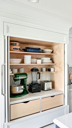 an open cabinet with bowls and mixers on it in a white kitchen, filled with dishes