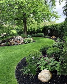 a garden with rocks and flowers in the center, surrounded by green grass and trees