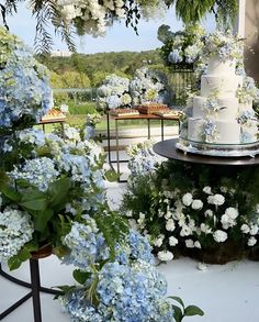 a wedding cake sitting on top of a table surrounded by blue flowers and greenery