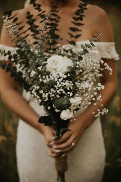 a woman in a white dress holding a bouquet of flowers and greenery on her wedding day