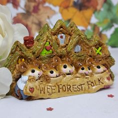 a figurine with three little animals on it next to a white flower and a sign that says wee forest folk