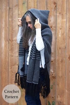 a woman standing in front of a wooden fence wearing a black and white ponchle