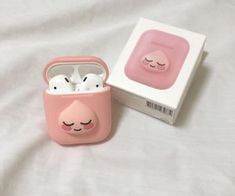 an airpods case sitting on top of a white bed next to a pink box