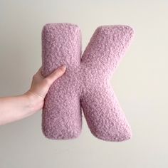 a person holding up a pink knitted letter k