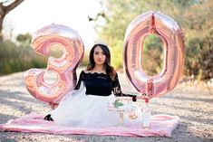 a woman sitting on a blanket with balloons in the shape of the number thirty three