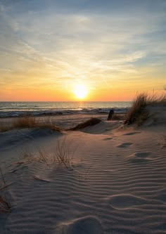 the sun is setting over the beach and sand dunes