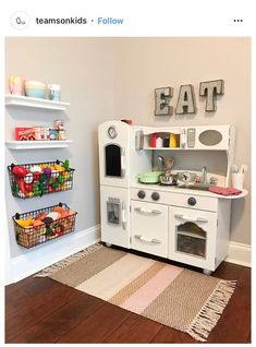 a white play kitchen with lots of food on the shelves and toys in baskets next to it