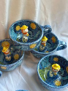 four blue and yellow dishes on a white tablecloth with one bowl holding three small figurines