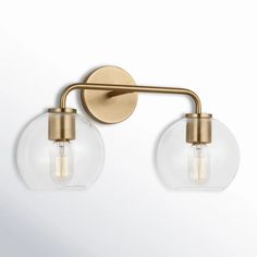 two light bathroom fixture with glass globes and brass finish on the wall, against a white background