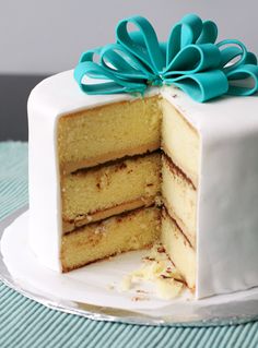 a white cake with three layers and a blue bow on top is sitting on a plate