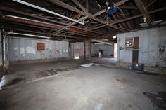 an empty room with no people in it and exposed pipes on the ceiling, next to a door