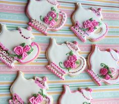 decorated cookies are arranged in the shape of tea kettles and pink roses on a striped tablecloth