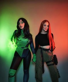 two beautiful women standing next to each other in front of a wall with green and red lights