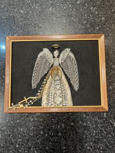 an embroidered angel in a wooden frame on a black background with gold trimmings