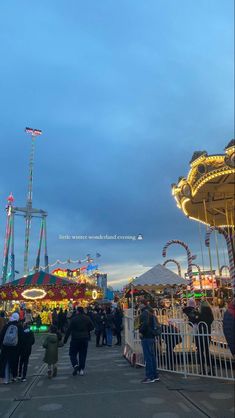 people are walking around an amusement park at dusk with rides and merry go round in the background