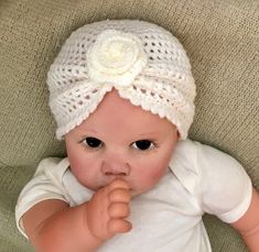 a baby wearing a white crochet hat with a flower on it's head