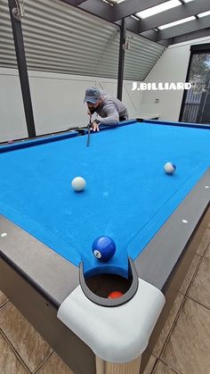 a man is playing pool with balls on a blue billiard table in an indoor area