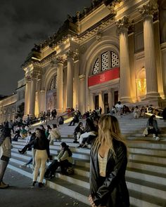 many people are sitting on the steps in front of an ornate building at night time