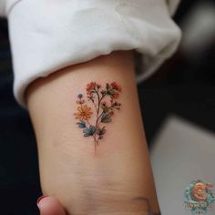 a small flower tattoo on the left side of the arm, with daisies and other flowers