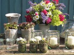 a table topped with vases filled with flowers next to candles and other glass containers