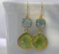 A peridot glass teardrop (15mm x 18.5mm) dangles from a aquamarine faceted cubic zirconia (13.5mm x 8mm) square in a gold plated brass setting. Overall length of earring approximately 1 1/2 inches.  Dangling from an elegant gold plated french ear wire. Includes plastic protectors.  Also available in silver, just put preference in notes to seller. All items ship in a gift box USPS first class mail. Wedding Gemstone Teardrop Earrings, Wedding Teardrop Gemstone Earrings, Lime Green Gemstone Wedding Jewelry, Lime Green Gemstone Jewelry For Wedding, Gemstone Teardrop Earrings For Wedding, Gold Teardrop Gemstone Earrings For Wedding, Wedding Gemstone Teardrop Dangle Earrings, Gemstone Dangle Teardrop Earrings For Wedding, Wedding Dangle Teardrop Gemstone Earrings