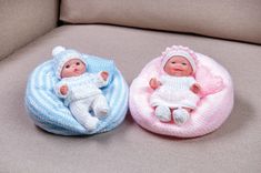 two small baby dolls sitting on top of a couch next to each other in knitted blankets