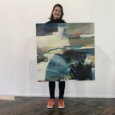 a woman standing in front of a painting holding up a large piece of art on the wall