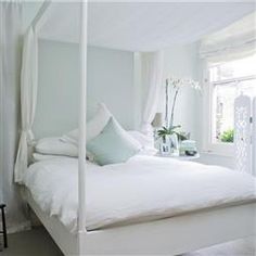 a white bed sitting in a bedroom next to a window with curtains on the windowsill