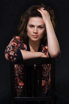 a woman sitting in a chair with her hand on her head and looking at the camera