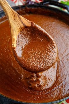 a wooden spoon full of brown sauce on top of a pan filled with chocolate pudding