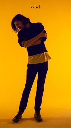 a woman standing in front of a yellow background with her hands on her hips and arms crossed