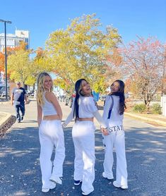 three girls in white outfits are walking down the street with their arms around each other