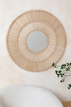 a round mirror hanging on the wall next to a white chair and potted plant