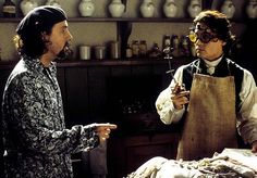 two men in an old fashioned kitchen talking to each other while holding utensils