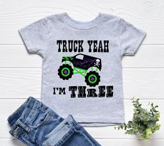 a shirt that says truck yeah i'm three on the front, and a pair of jeans next to it