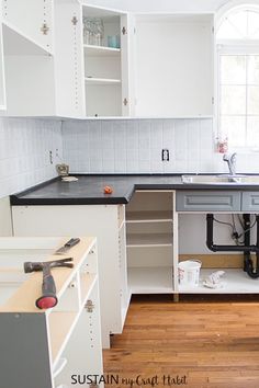 an unfinished kitchen with white cabinets and black counter tops is pictured in this image, there are tools under the sink