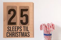 a wooden sign that says 25 sleeps til christmas with candy canes in the foreground