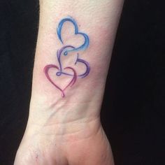 a small tattoo on the wrist of a woman with two hearts in blue and pink