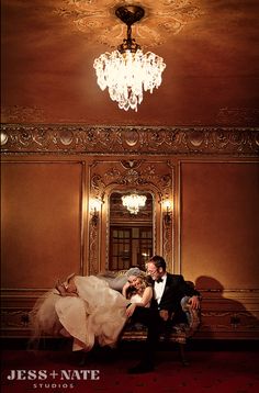 a bride and groom sitting on a bench in the middle of a room with chandelier